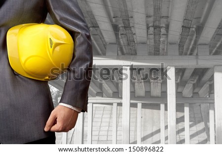 worker or engineer holding in hands yellow helmet for workers security on the background of a new concrete bridge over the river in perspective buildings gray idea    building new road junctions