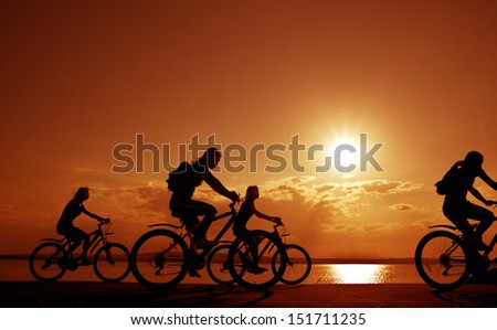 Image of sporty company four friends on bicycles outdoors against sunset. Silhouette A lot phases of motion of a single cyclist along the shoreline coast Reflection on water Space for inscription