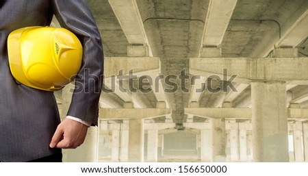 worker or engineer holding in hands yellow helmet for workers security on the background of a new concrete bridge over the river in perspective buildings gray idea   building new road junctions
