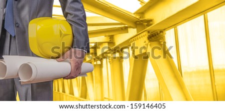 worker or engineer holding in hands yellow helmet for workers security on the background of a new metal bridge over the river in perspective buildings gray idea  building new road junctions