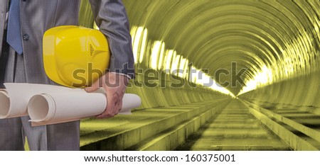 engineer yellow helmet for workers security with construction plans against background of an underground mine with arc legs and rails for trolleys with coal