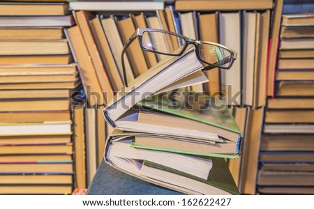 open and closed books and black glasses on table front of a full bookshelf September 1st - the day of knowledge symbol of vision loss and eye strain from long reading