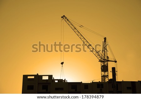 Background of Construction site with home silhouette manual worker in helmet disengages from the cargo hook on the construction crane slings on yellow sun set cloudy sky with rays light  backdrop