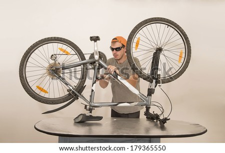 Mechanic or serviceman in orange cup and sunglasses installing wheel on a bicycle in workshop Young man repairing bicycle with big wrench , isolated on white background