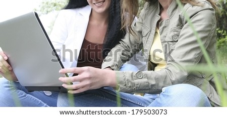 Two beautiful girl on laptop computer outdoors. Sit outdoor on green grass.No face Unrecognizable person