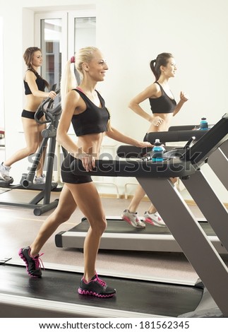 Three young adult sporty women run on machine in the gym centre  girl friends on Treadmill running inside in fitness gym