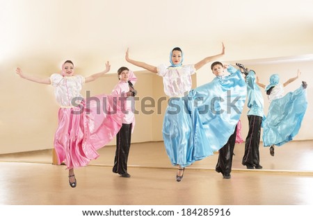 Beautiful group - four people dancer girls and man jumping in pink and blue folk costume dances performing new folk russian or ukraine dance near yellow wall with mirror reflection