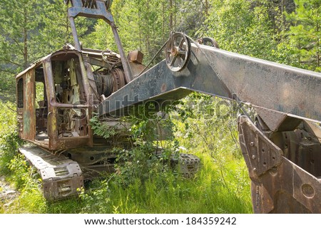 Abandoned old rusty excavator in summer fresh green forest and grass