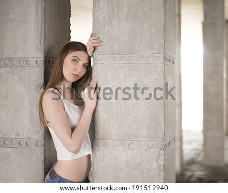 Portrait of Pretty brunette woman in white shirt against an architectural concrete beam background Fashion beautiful dreaming girl looking at camera Copy space for inscription