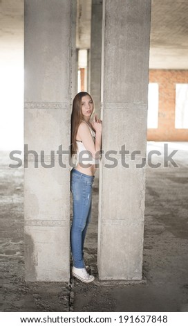 Portrait of Pretty brunette woman in white shirt against an architectural concrete beam background Fashion beautiful dreaming girl looking at camera Copy space for inscription