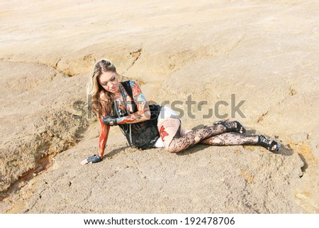 Portrait of beauty freak girl with bat and with body art on her hand on empty land desert background woman painted body art in form of fire in white t-shirt and denim shorts and torn pantyhose