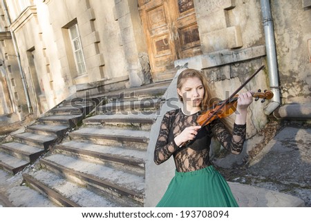Portrait of Young adult sexy girl with long brown hair with a broken violin on old retro stairway  in the Gothic style of classicism building background Caucasian woman in black transparent shirt