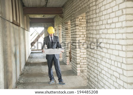Full length architect looking comparing blue print paper plan housing project with building wearing yellow helmet Back view businessman in perspective long corridor with door perspective background