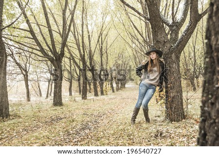 Outdoors portrait of casual clothed gorgeous fall fashion girl on green and yellow autumn snowy park background Cute slim woman based on cold tree and looking at camera