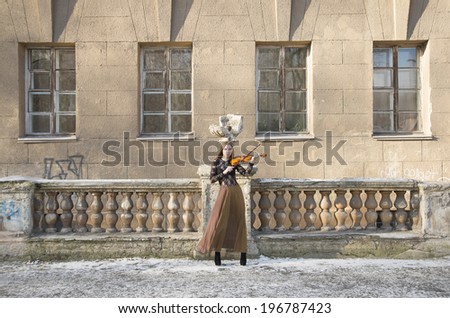 Full length portrait of Young adult sexy woman with long hair playing on broken violin on old retro fence and wall with windows in the Gothic style of classicism archtect backdrop