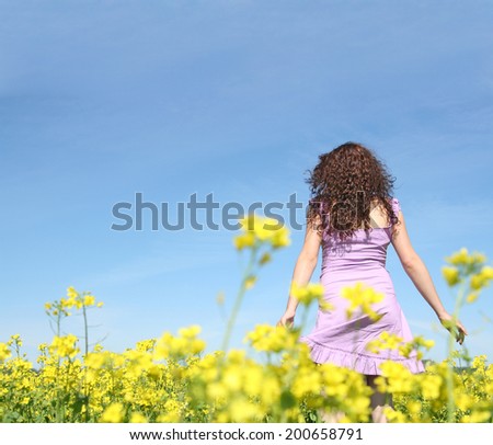 Back view redhead curly young adult woman in yellow raps flower field and blue cloudy sky background Copy space for inscription Girl wearing violet sexy dress No face