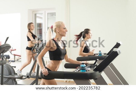 Portrait of Three young adult sporty women run on machine in the gym centre girl friends on Treadmill running inside in fitness gym Copy space for inscription
