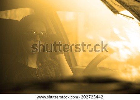 woman in car indoor keeps wheel turning around serious looking through idea taxi driver holding sunglasses in hands with leather black gloves against sun set sky background Copy space for inscription