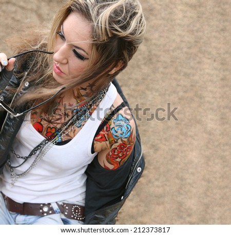 Portrait of stylish tattoo woman painted body art in form of blue flower in shirt, ta too Girl wearing black leather jacket holding sunglasses on texture background Empty copy space for inscription