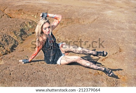 Portrait of beauty freak tattoo girl with bat and with body art on her hand on empty land desert background woman painted body art in form of fire in white shirt and jeans shorts and torn pantyhose