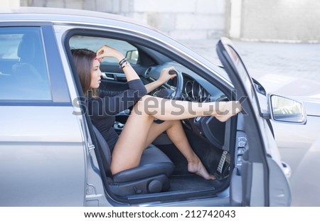 Portrait of babe Young adult sexy brunette dreaming girl sitting in luxury black car Slim cute asian woman listening music inside black leather luxury chair auto open door with leg Fingers on forehead