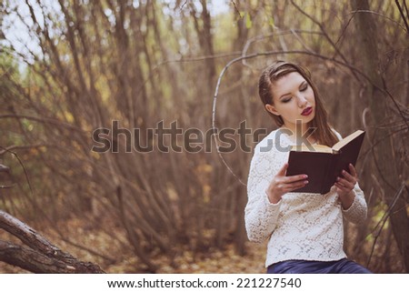 woman with long wet hair in the autumn forest reading big book  Girl sit on trunk in fall park and looking at page  Empty copy space for inscription Female wearing white transparent shirt under rain