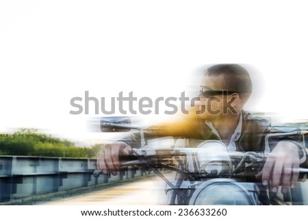 Romantic blur portrait handsome biker man in sunglasses sits on a bike on a sunset on old rusty metal bridge in city against house and sunny sky background Empty copy space for inscription