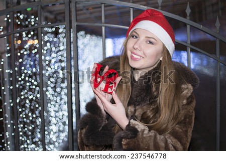outdoor outside portrait of happy young Christmas woman with Santa Claus red hat Blue bokeh blur light effect. Cute girl with smiley face looking at camera Female holding fur collar coat  Night light