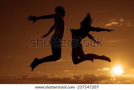 family vacations on the beach Silhouette of a couple - man and woman jumping on the beach on sunset clouds sky with orange sun background with reflection on yellow  splash water texture
