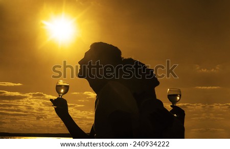 Silhouettes of Man and woman drink glasses of champagne wine at sunset dramatic yellow sky with clouds background Empty Copy space for inscription Couple against sun shine rays