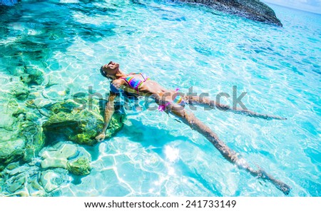 Slim hot sexy tanned skin woman Swimming Bikini Swimmer Cute young adult girl lie on back in blue water texture with shadow on white sand bottom Sun light in perspective ocean or sea