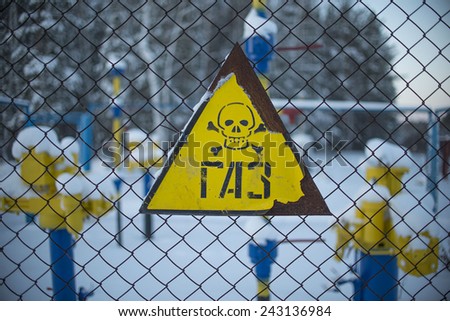 Yellow sign with skull and bones gas underground storage, refinery factory Part of snowy yellow blue pipe with valve Metal rusty sign  Outdoor on winter forest background