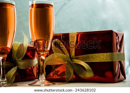 Red gift boxes with golden ribbon , two wine glasses with champagne on blue gray background Empty space for inscription