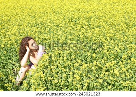 Beautiful caucasian young adult redhead curly woman in short purple dress sit on summer yellow green flower rape field outdoors at sunny day Full length Empty Copy space for inscription Closed eyes