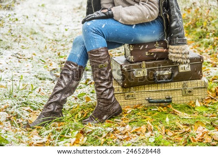 no face person travel Stylish slim woman wait for something on three retro old fashion suitcases Copy space for inscription Girl sit on leather case on grass autumn leaves and snowflakes background