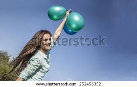 Windy day summer portrait of Beautiful cute woman wear casual blue dress flying on balloons Wind weather Latin Hispanic free girl with smiley tanned face against blue spring sky