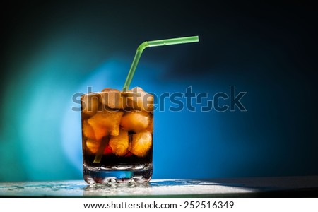 Object of glass transparent full glass with in form star ice cubes and Coke with a green and yellow tube on blue background Empty space for inscription