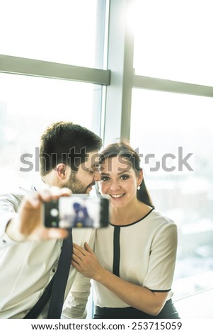 Focus on eyes cheerful couple embrace and taking a selfie with a smartphone Man and woman look at mobile phone screen Sun light shine in window glass with plastic frame Empty space for inscription