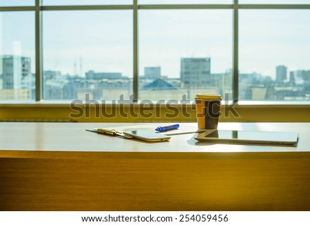 Object tools in office room tablet computer paper cup with hot coffee Cell mobile phone Paper document lie on wooden table against blue sky window with houses Empty space for inscription