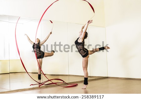 Portrait of cut Pretty rhythmic gymnast girl exercising with red ribbon with reflection on mirror yellow wall background Caucasian Woman in sexy lace transparent suit, woolen golfs stand on one leg