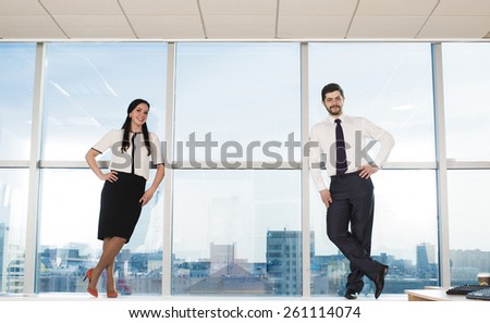 Businessman and businesswoman stand full length on floor near modern office window against urban view big city center houses on background Man and woman wear black white well formal business dress