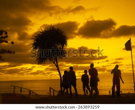 After Party young adult people on hot evening summer coast beach on yellow or orange dramatic sunset sky with clouds  background Gays talking at mobile cell phone Kids swim in ocean against horizon