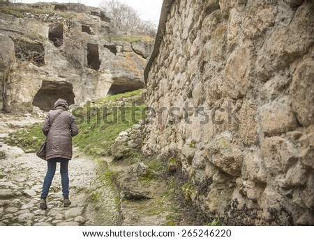 tourist woman stand near old retro vintage aged historical stone wall texture Back view full length girl walk along history fence Empty copy space for inscription