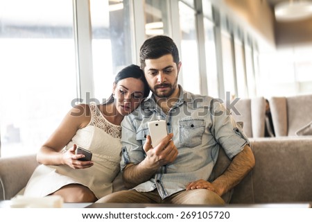 Serious Couple love sit on sofa couch look at smart phone Woman show screen with image or site Family, technology internet and happiness concept concentrated couple with smartphones at free wi fi cafe