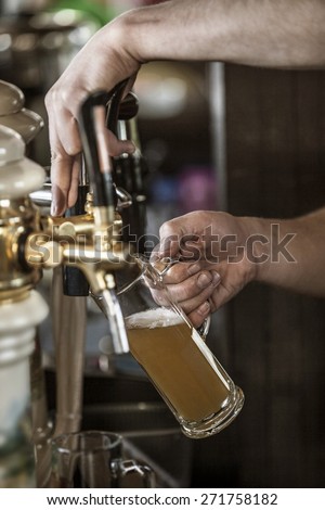 Close up of the hand of a man pouring a tankard of frothy draught beer from a stainless steel beer tap in a bar or pub into a large glass tankard