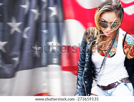 Portrait of stylish tattoo woman painted body art in form of blue flower on skin, ta too Girl wear black leather jacket modern sunglasses on american flag  background Empty copy space for inscription