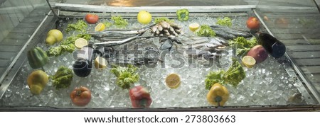 Row food showcase in a restaurant or shop with fish fruit and vegetable - red paprika lemon green salad tomatoes apple and one bottle vine Seafood lie inside fridge in ice