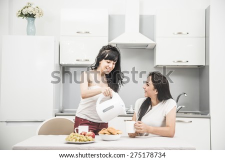 Couple of lesbian Girls Enjoy coffee at home taking about something Two young adult beautiful women drink tea in modern kitchen white interior and gossip Asian housewife pour water from plastic teapot