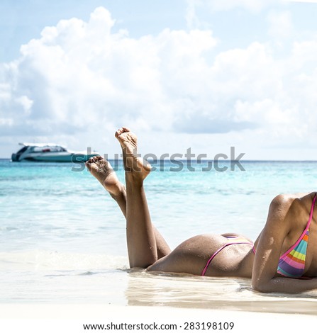 Unrecognizable person young adult girl Exotic Hideaway Tanning Pleasure no face woman with beautiful tanned brown skin body on a tropical white sand beach on blue sky with clouds Yacht on horizon