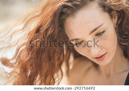 Summer sad portrait, beautiful freckled young adult girl with red hair look at camera Cute curly redhead woman with hand near face against outdoor background Empty space for inscription